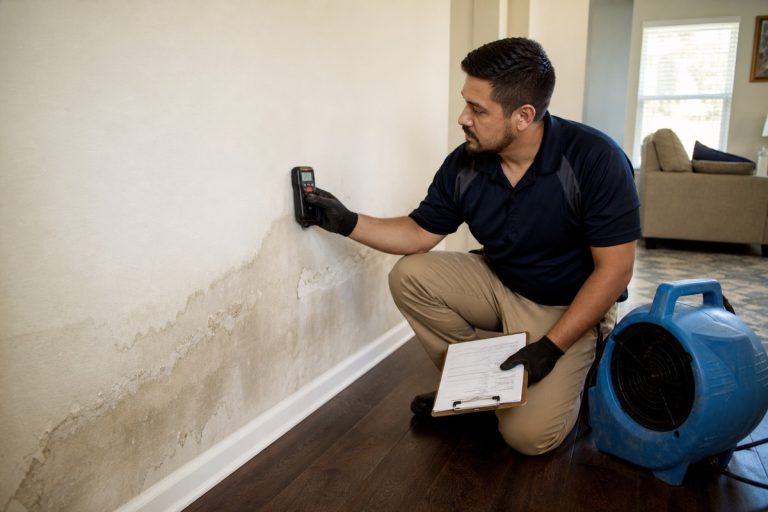 Water damage restoration technician using a moisture meter on a water-stained wall in a Houston home