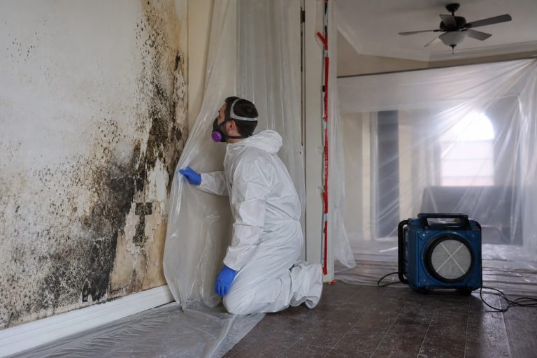 Mold remediation technician in protective gear setting up containment in a Houston home